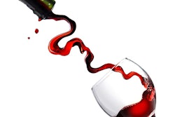 Pouring red wine in glass goblet isolated on white