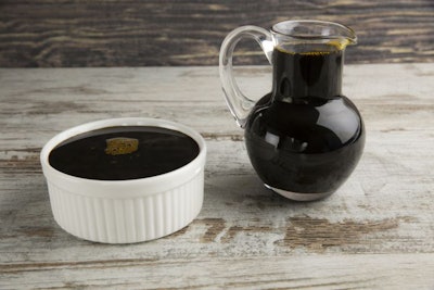 Grape molasses in bowl and glass pitcher on wooden background.