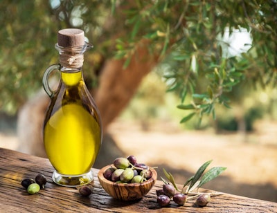 Bottle of olive oil and olive berries are on the wooden table un