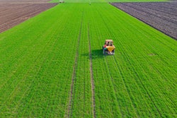 Above View On Tractor As Throws, Fertilizing Arable Farmland Wit