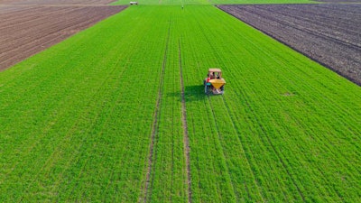 Above View On Tractor As Throws, Fertilizing Arable Farmland Wit