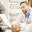 Serious experienced bearded male engineer in lab coat explaining production data to colleague while they thinking of factory automation