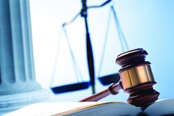 A gavel rests on top of an open law book with a justice scale and a Greek column in the background.