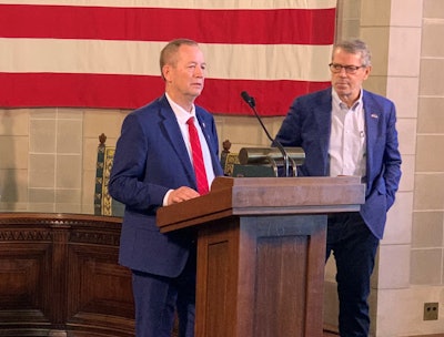 Nebraska Sen. Barry DeKay talks about legislation to prohibit the creation, distribution and sale of cultivated meat, while Gov. Jim Pillen looks on.