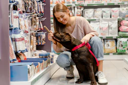 Uma mulher oferecendo um petisco para seu cachorro, que aparenta ser um labrador marrom, em um pet shop.