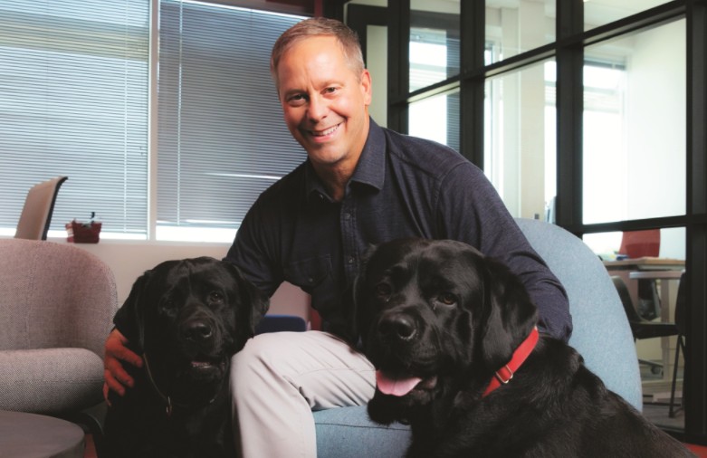Smiling professional sitting with two black Labrador dogs in an office