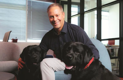 Smiling professional sitting with two black Labrador dogs in an office