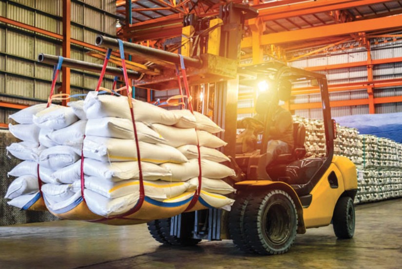 Yellow forklift lifting stacked white sacks in industrial warehouse with overhead crane