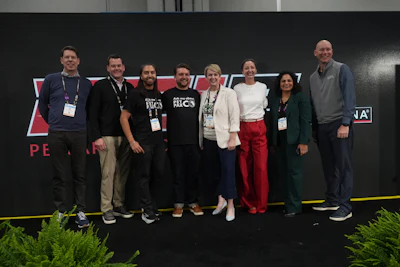 Eight professionals wearing conference badges pose together at a branded event backdrop
