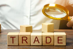 Magnifying glass examining wooden blocks spelling 'TRADE' on a desk