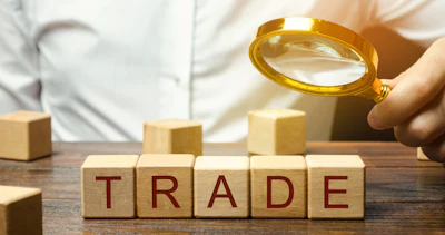 Magnifying glass examining wooden blocks spelling 'TRADE' on a desk