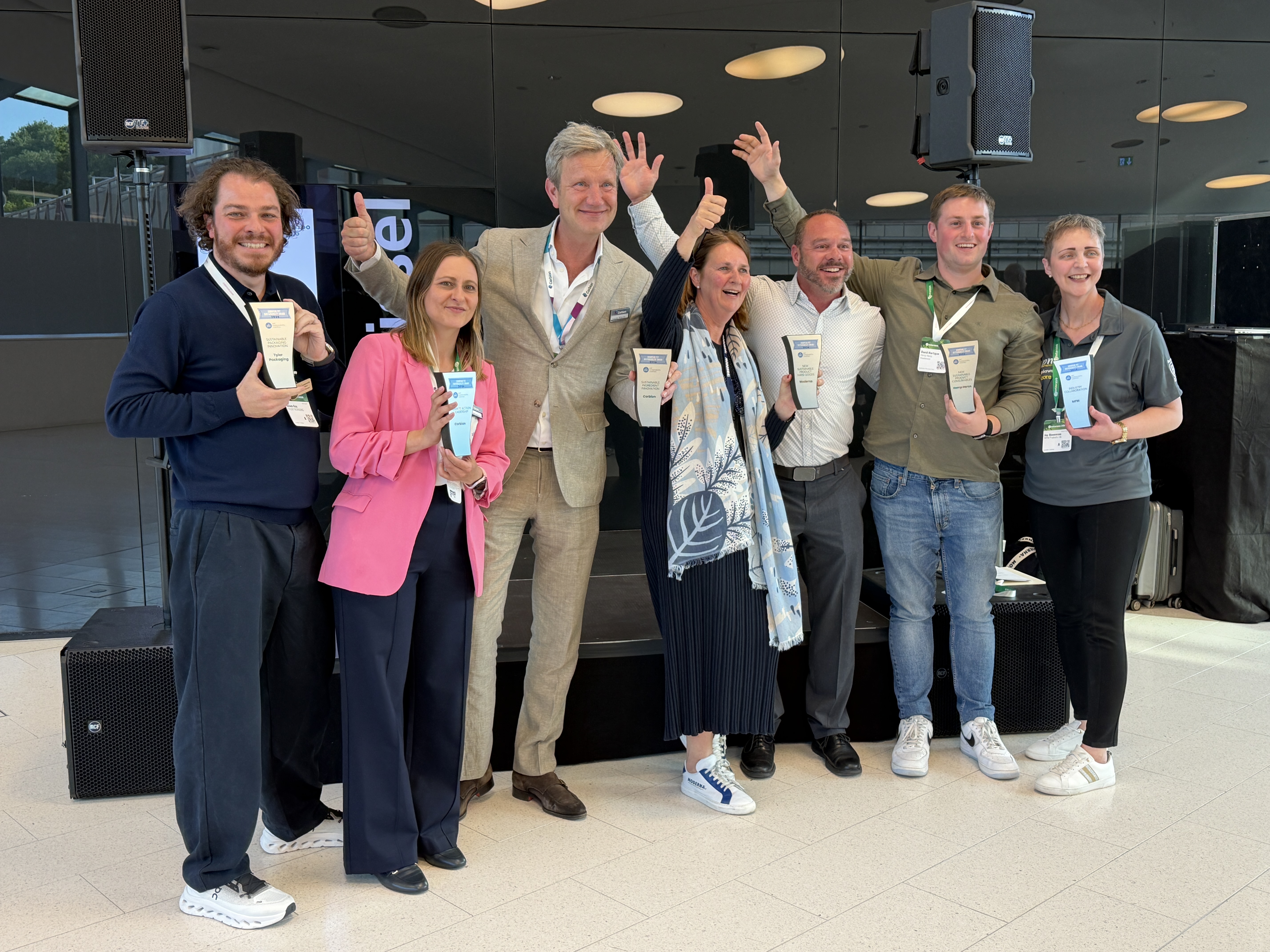 Team of eight professionals celebrating at a corporate conference event, wearing name badges and lanyards