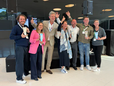 Team of eight professionals celebrating at a corporate conference event, wearing name badges and lanyards
