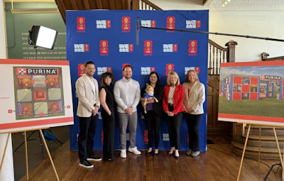 Group of seven people posing at Purina corporate event with branded backdrop and display boards