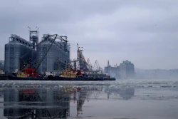 Industrial port facility with grain elevator, cargo cranes, and docked vessel on frozen waterway under cloudy sky