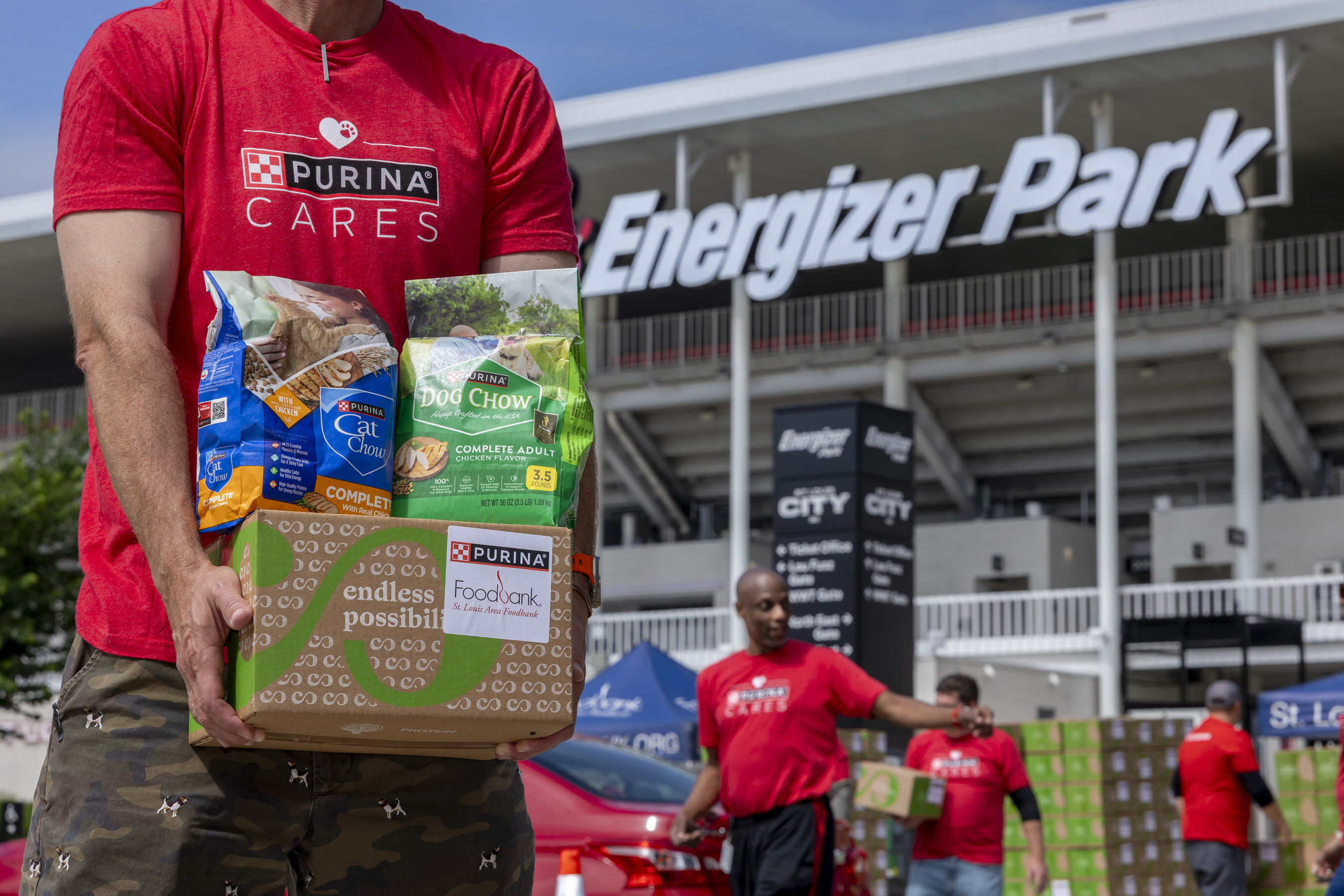 Volunteer in red Purina Cares shirt holding pet food donation box at Energizer Park stadium event
