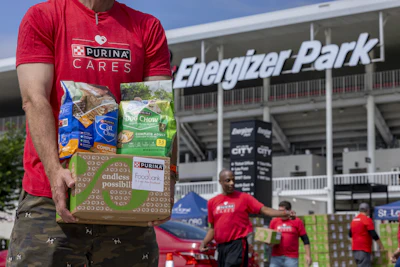 Volunteer in red Purina Cares shirt holding pet food donation box at Energizer Park stadium event