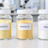 Three glass jars labeled Vitamin K, Vitamin A, and Niacin containing supplement powders in a laboratory setting