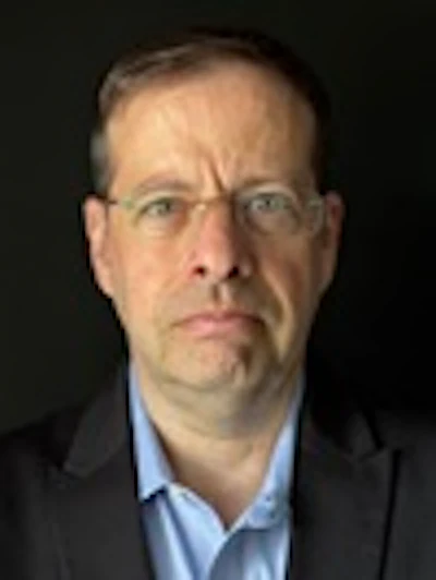 Professional headshot of a man wearing glasses and blue shirt against dark background