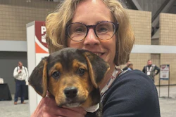 Woman wearing glasses holding a tricolor beagle dog at an indoor event venue