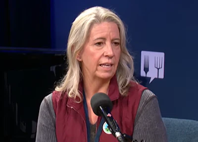 Woman speaking into microphone during podcast interview with blue background