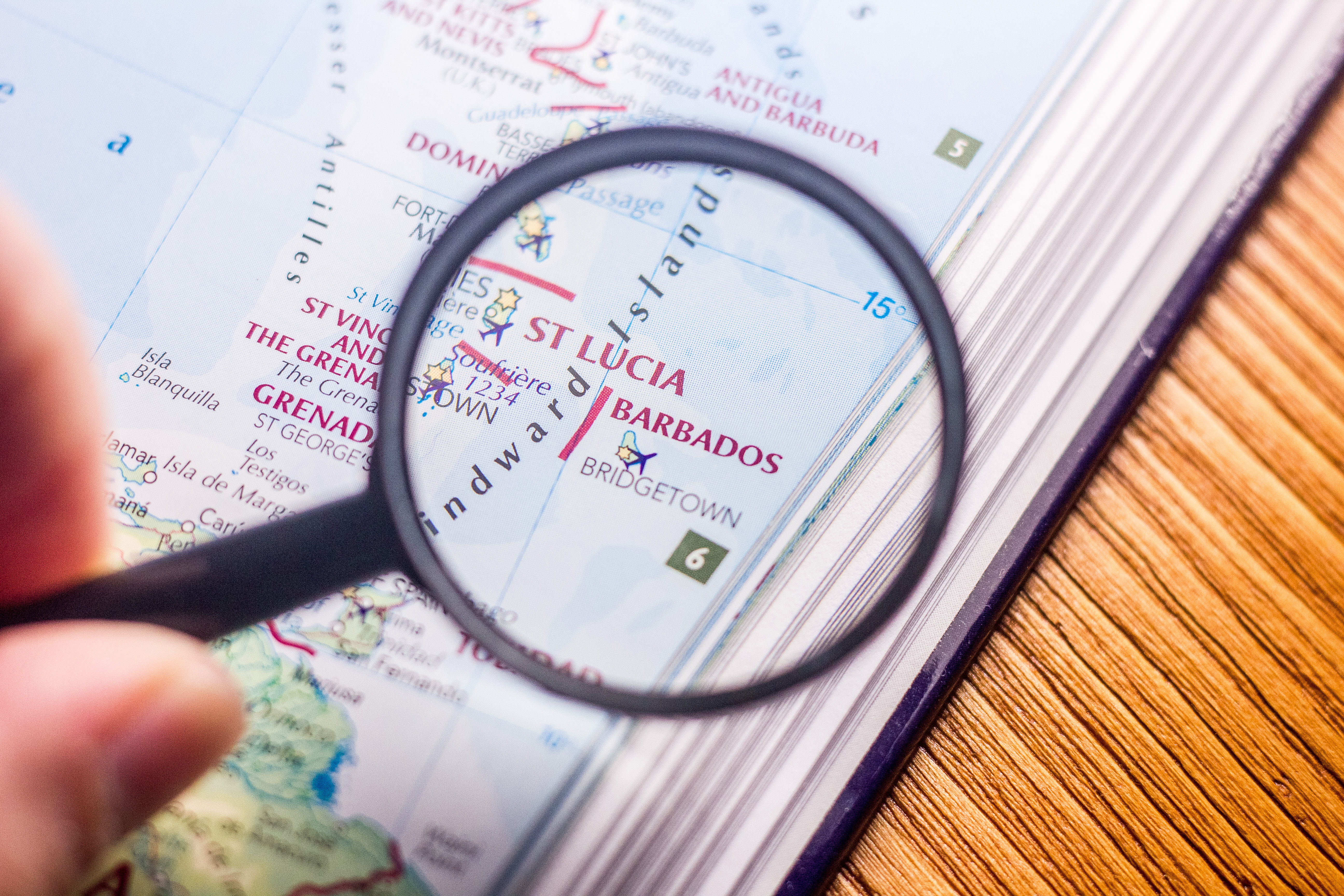 Magnifying glass examining a map showing St Lucia, Barbados, and Bridgetown on an atlas page