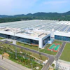 Aerial view of modern industrial facility with solar panel roof, sports courts, and surrounding green fields