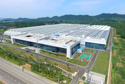 Aerial view of modern industrial facility with solar panel roof, sports courts, and surrounding green fields
