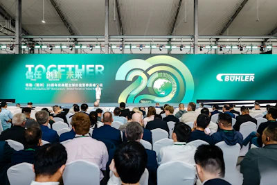 Large conference audience seated facing turquoise stage banner celebrating 20 years with Bühler branding