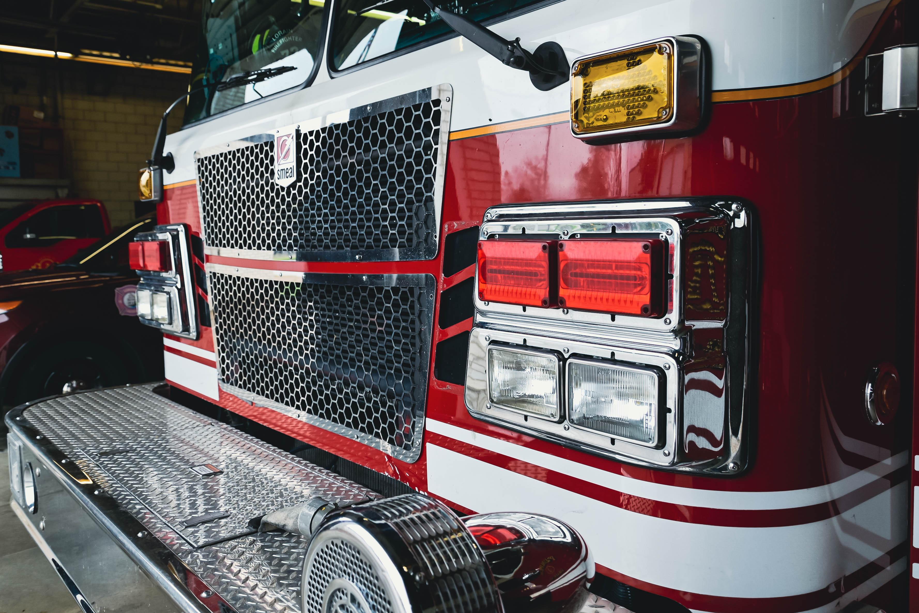 Red and white fire truck front with hexagonal grille, headlights, and emergency equipment in garage