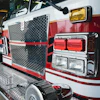 Red and white fire truck front with hexagonal grille, headlights, and emergency equipment in garage