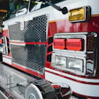 Red and white fire truck front with hexagonal grille, headlights, and emergency equipment in garage