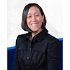 Professional headshot of a smiling woman wearing a black button-up shirt against a white background with blue accent