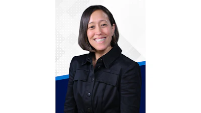 Professional headshot of a smiling woman wearing a black button-up shirt against a white background with blue accent