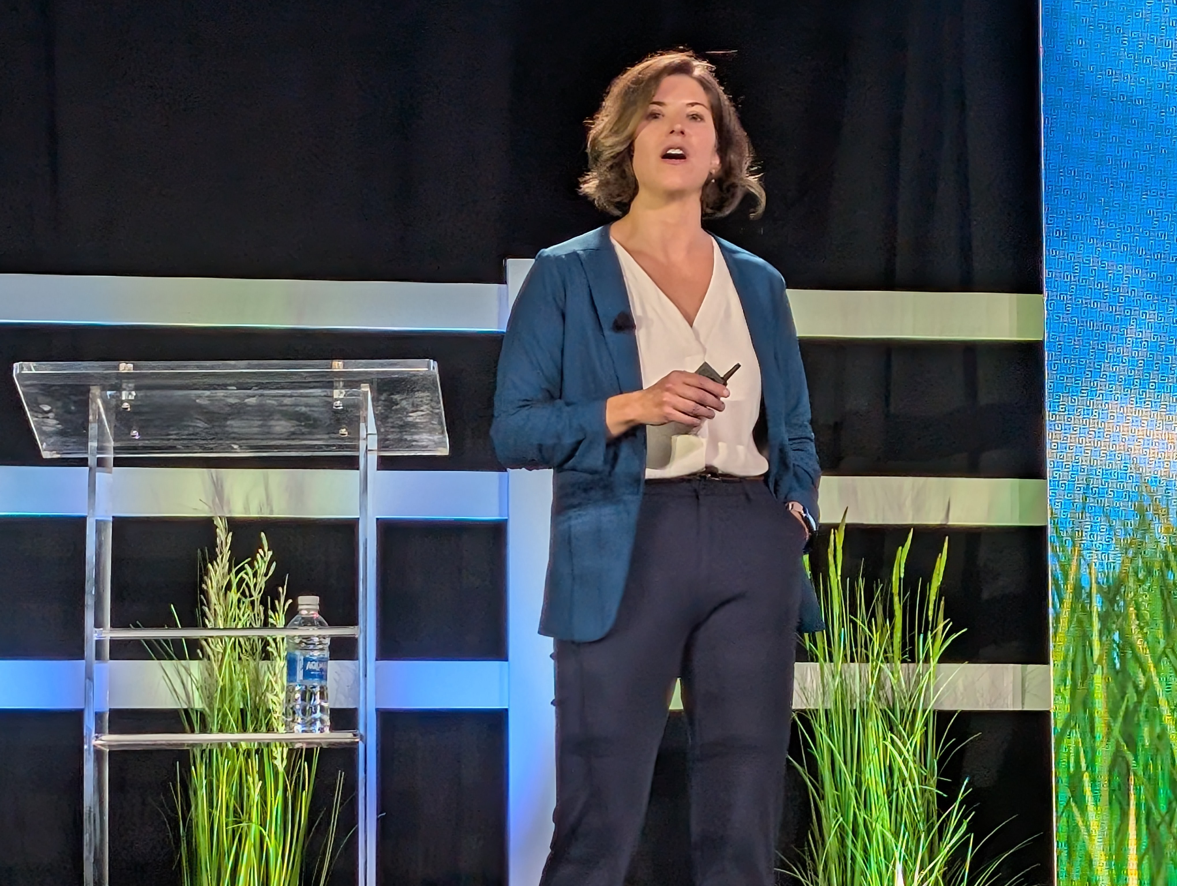 Professional woman presenting on stage at corporate event with modern striped backdrop and green plants