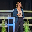 Professional woman presenting on stage at corporate event with modern striped backdrop and green plants