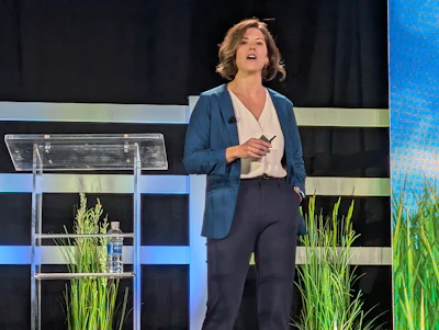 Professional woman presenting on stage at corporate event with modern striped backdrop and green plants