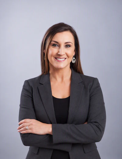 Professional headshot of a smiling woman in dark blazer with crossed arms