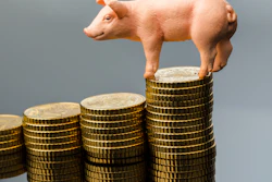 Piggy bank figurine standing on stacked gold coins in ascending columns against gray background