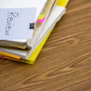 Notebook with 'Review' written on page, yellow highlighter, sticky notes, and binder clip on wooden desk