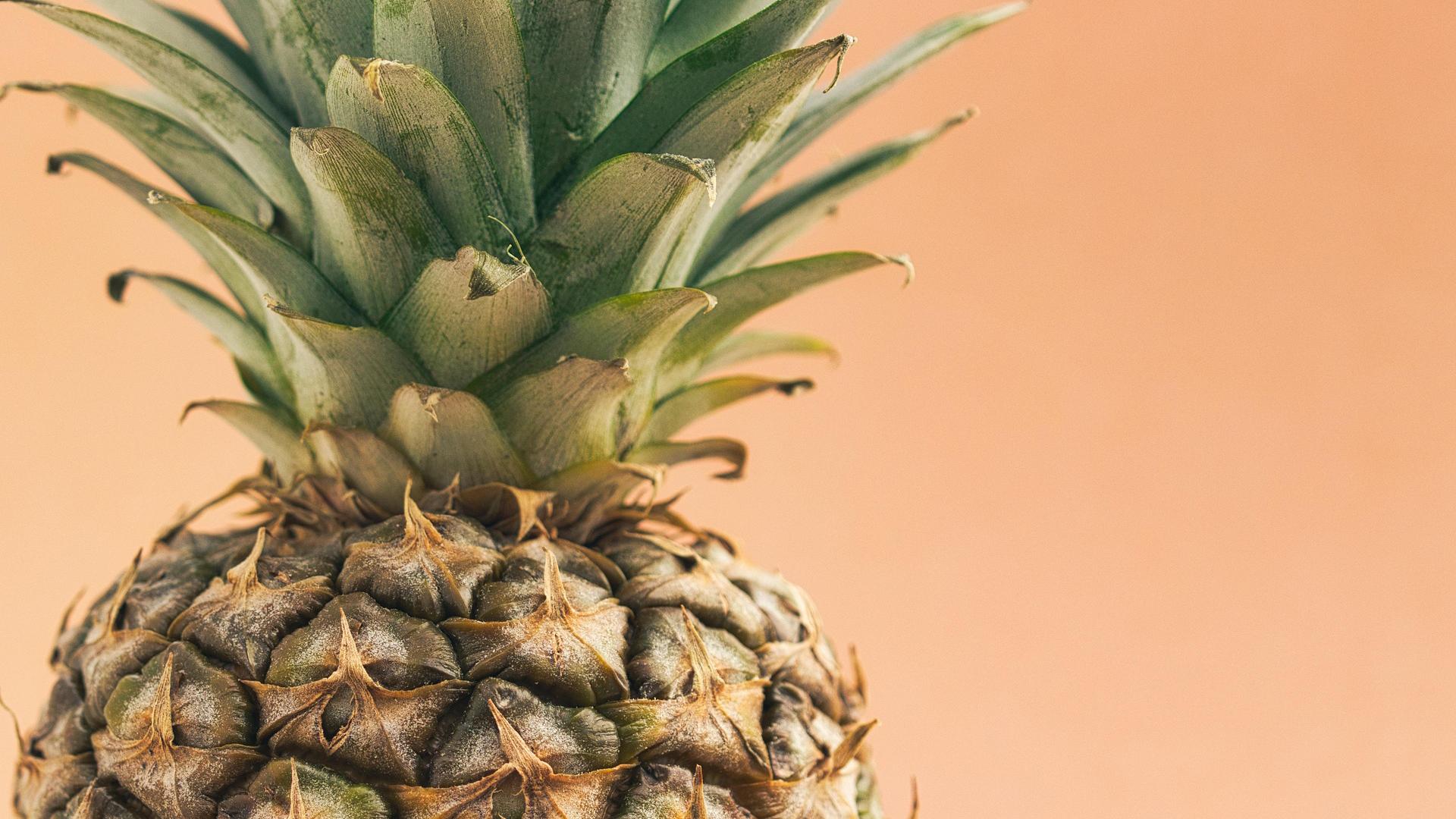 Close-up of fresh pineapple with green crown leaves against warm peachy background