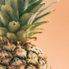 Close-up of fresh pineapple with green crown leaves against warm peachy background