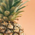 Close-up of fresh pineapple with green crown leaves against warm peachy background
