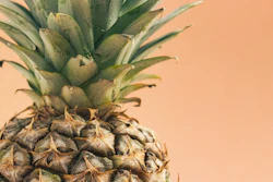 Close-up of fresh pineapple with green crown leaves against warm peachy background