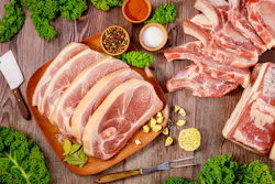 Raw pork chops and meat cuts arranged on wooden boards with fresh kale, lemon slices, and seasoning bowls