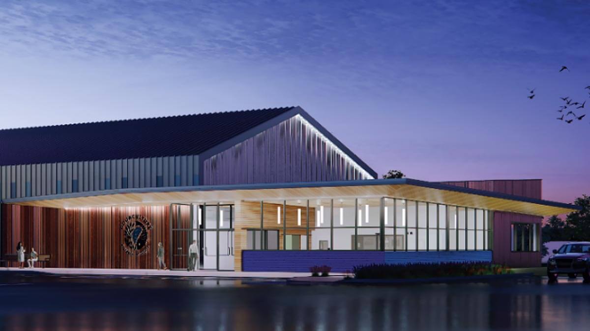 Modern waterfront building with pitched roof, wood and metal cladding, illuminated glass facade at dusk