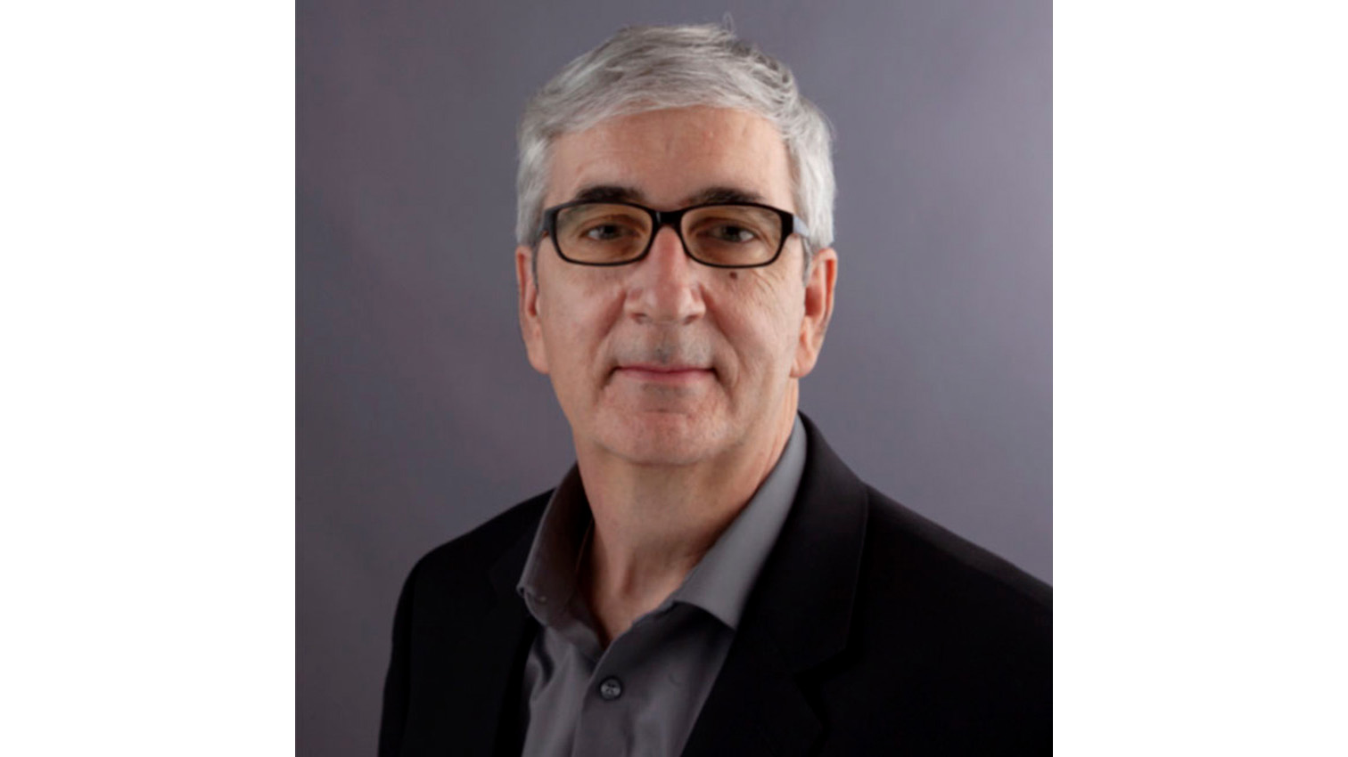 Professional headshot of a man with gray hair wearing glasses and dark blazer over gray shirt