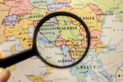 Magnifying glass examining a map of the Balkans region showing Serbia, Bosnia, Kosovo, and surrounding countries