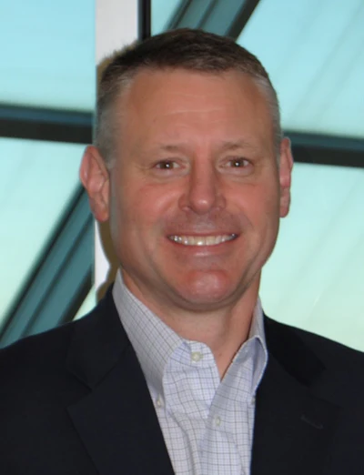 Professional headshot of a smiling man in dark blazer and light checkered shirt